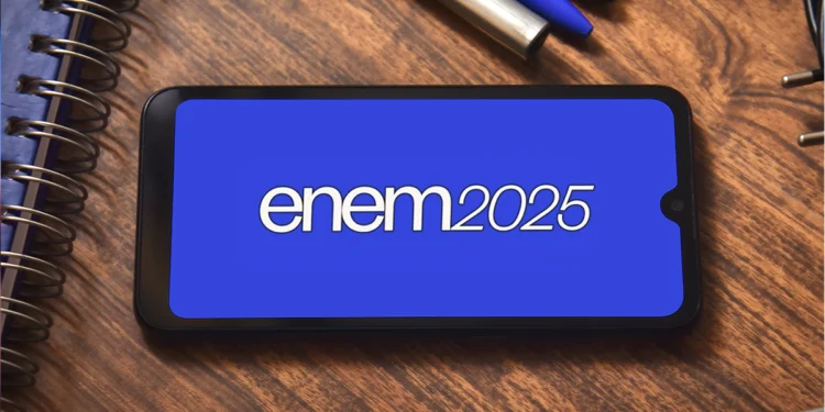 Tela de celular exibindo o logotipo do ENEM 2025 sobre uma mesa com cadernos e canetas.