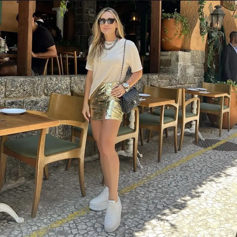 Mulher usando um look casual com blusa branca e shorts metalizados, combinando com tênis branco e bolsa preta.
