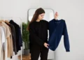 Mulher analisando um suéter azul enquanto escolhe roupas, ilustrando como diferentes cores podem influenciar a autoestima.