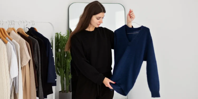 A Psicologia sugere que essas 5 cores podem estar ligadas à baixa autoestima 1 Mulher analisando um suéter azul enquanto escolhe roupas, ilustrando como diferentes cores podem influenciar a autoestima.