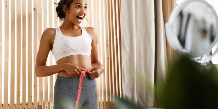 Mulher feliz medindo a cintura após alcançar progresso no treino para o verão.