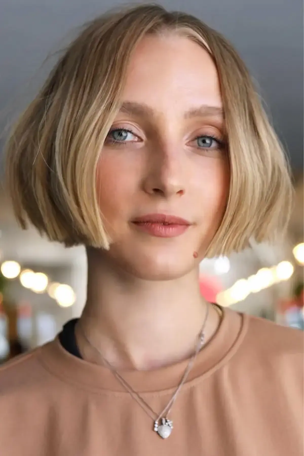 Mulher com corte de cabelo Micro Bob, em tons loiros, com um estilo moderno e elegante, destacando o corte na altura do lóbulo da orelha.