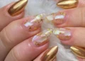 Nail art sofisticada com unhas douradas e detalhes transparentes com folha de ouro.