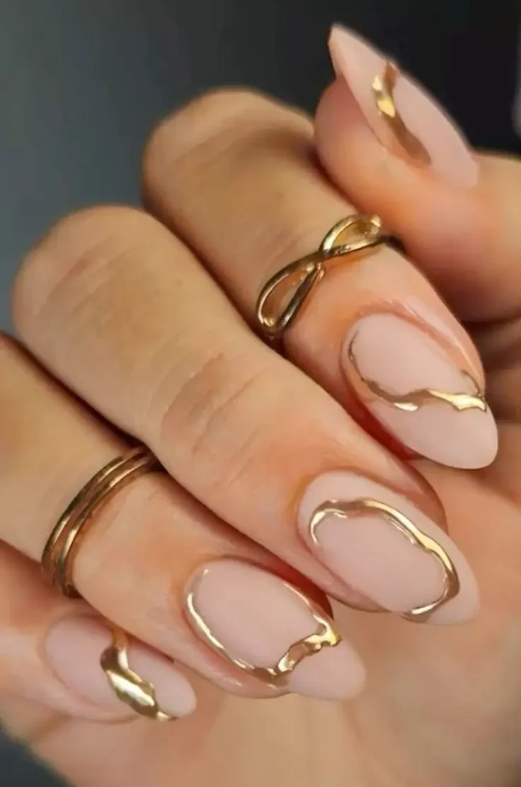 Unhas nude com detalhes dourados, criando um design sofisticado e minimalista.