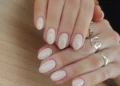 Unhas curtas com esmalte nude e acabamento brilhante, com anéis dourados delicados, ideal para um visual discreto e sofisticado.