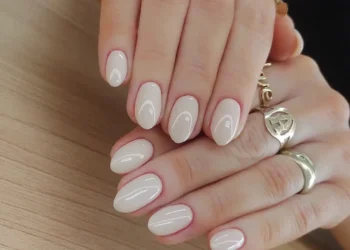 Unhas curtas com esmalte nude e acabamento brilhante, com anéis dourados delicados, ideal para um visual discreto e sofisticado.