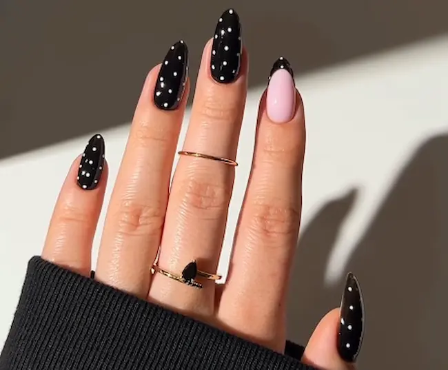 Unhas estilo poá com base preta e pontos brancos, combinando com uma unha rosa delicada.