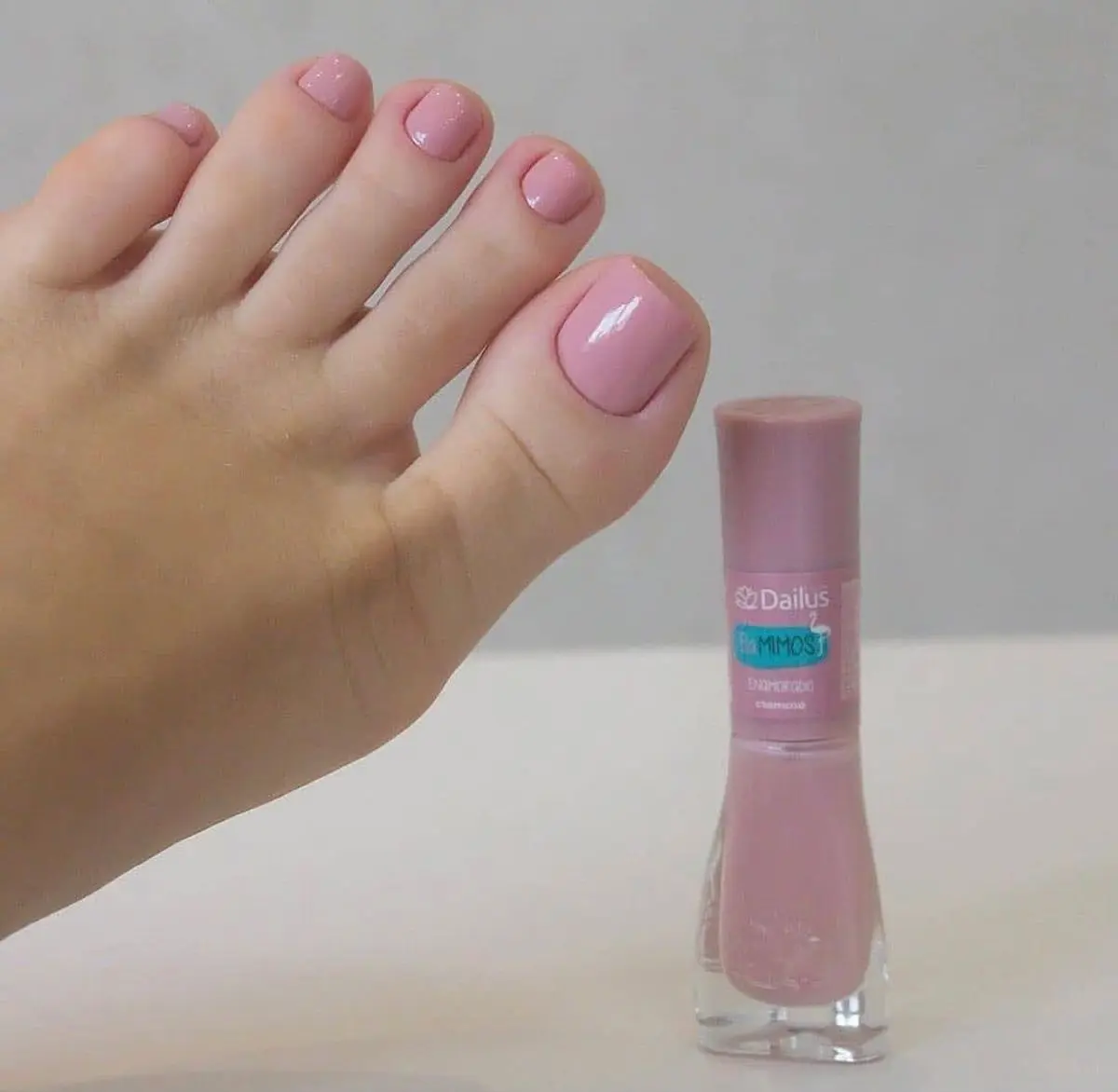 Cores de esmalte para os pés que serão tendência no verão 2026; renove seu visual 6 Unhas dos pés com esmalte rosa claro delicado ao lado de frasco de esmalte.