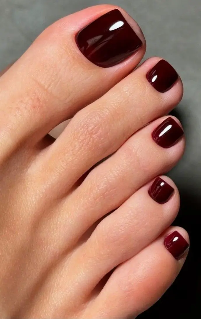 Cores de esmalte para os pés que serão tendência no verão 2026; renove seu visual 2 Close-up de pés com esmalte vinho escuro em acabamento brilhante.